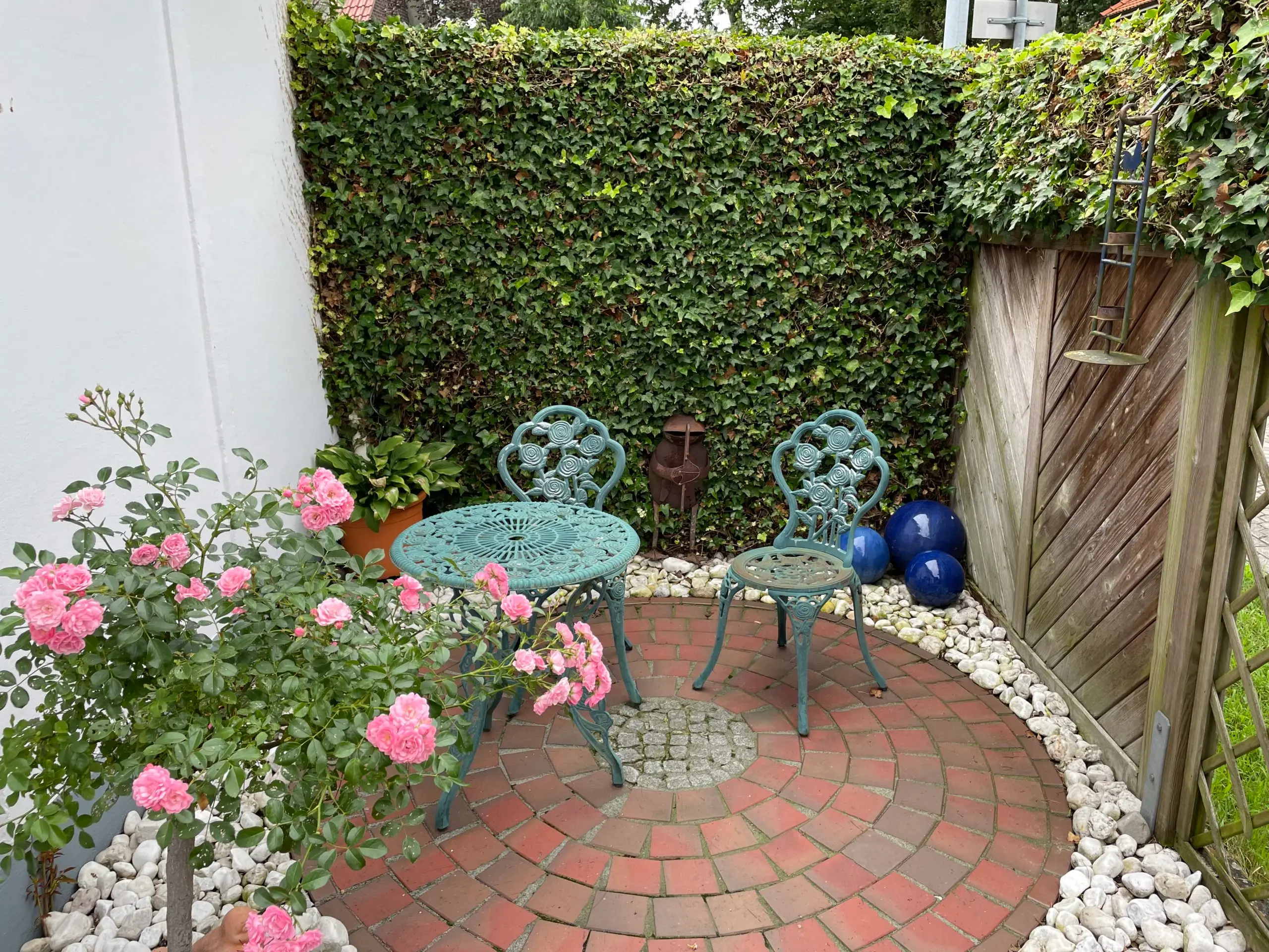 Sitzecke im Garten mit Rosen vor einer grünen Hecke